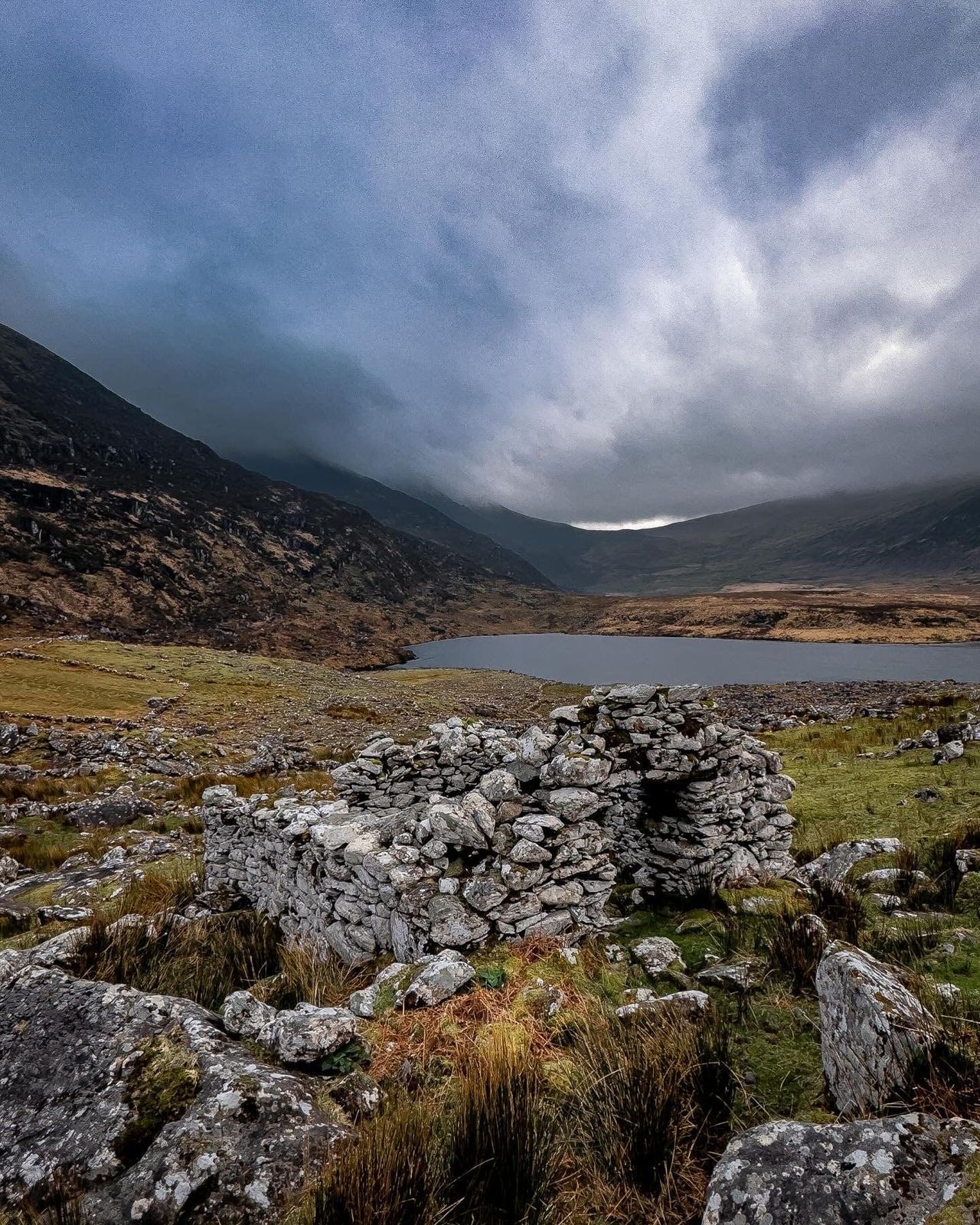 Old stone ruins beside a mountain lake under dark cloud
