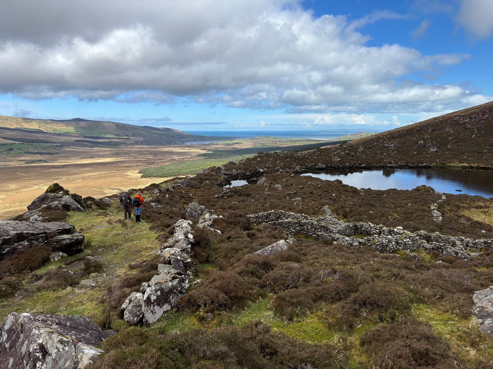 Walkers following stone walls above a small mountain lake