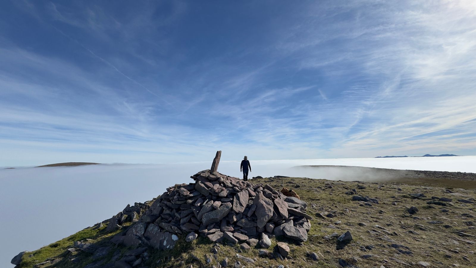 A walker and cairn above cloud with a circular glory in the mist