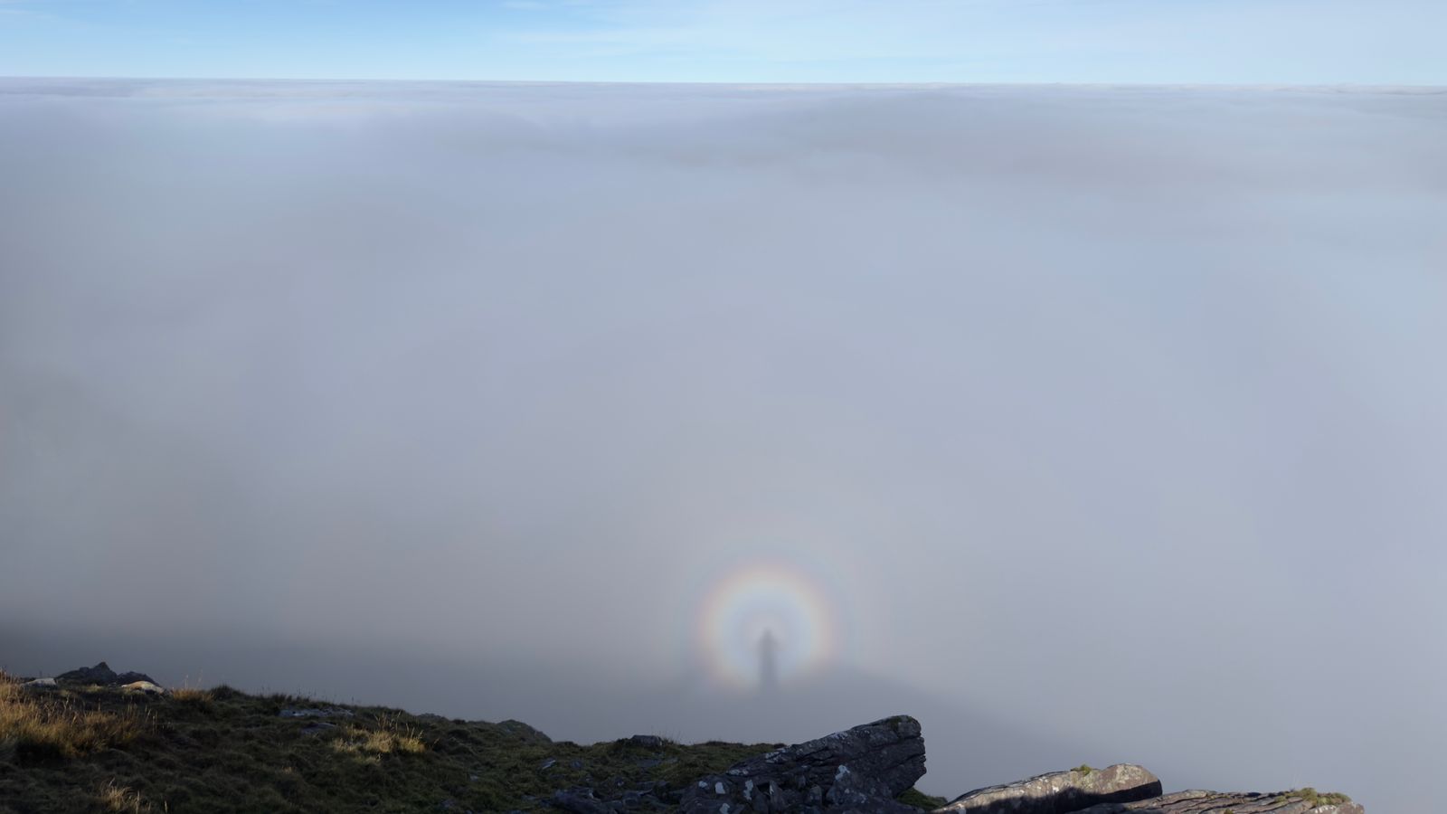 A pale glory forming in cloud below the mountain