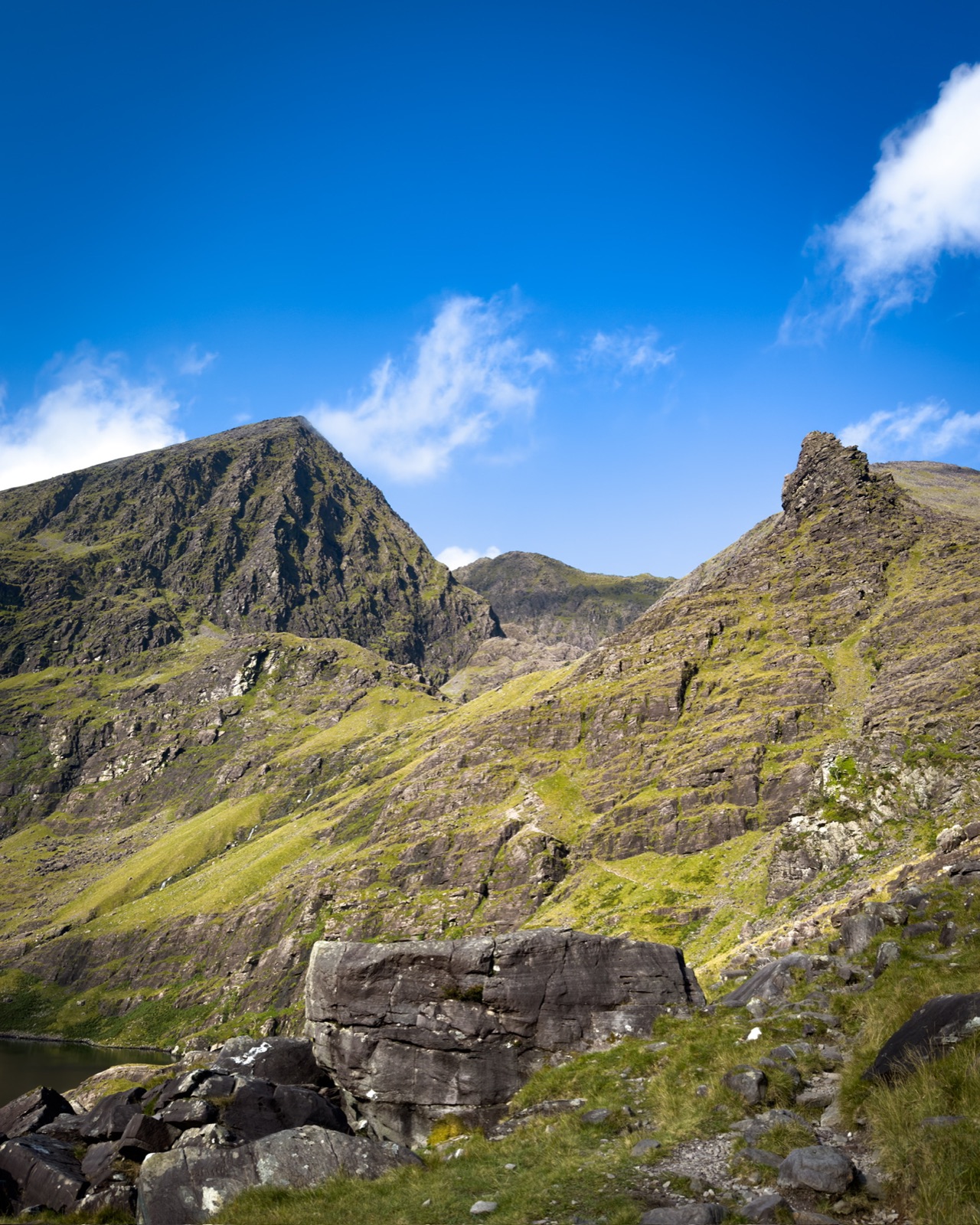 Rocky mountain walls rising above Lough Cummeenoughter under a blue sky