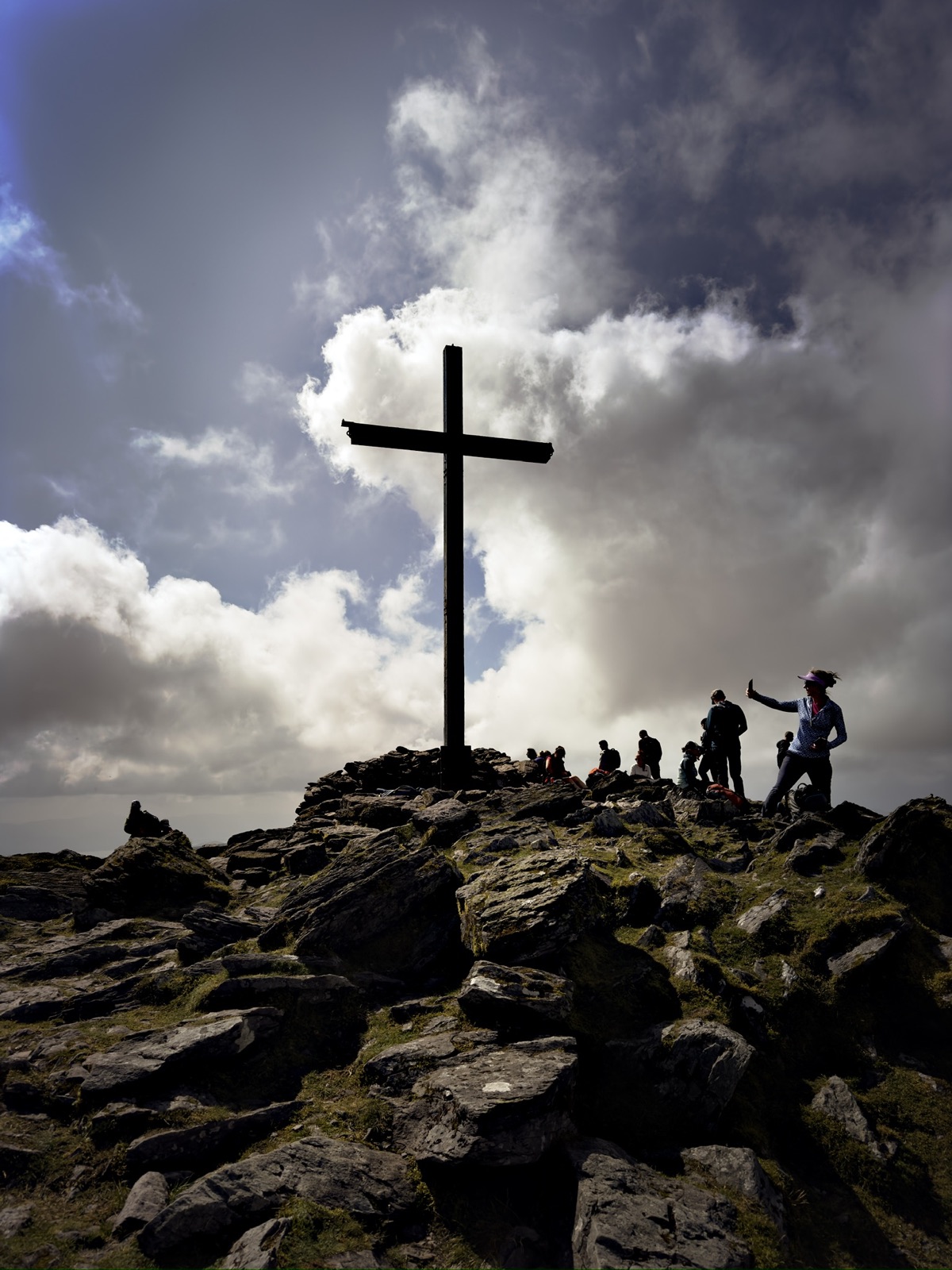 Hikers beside a summit cross silhouetted against dramatic cloud