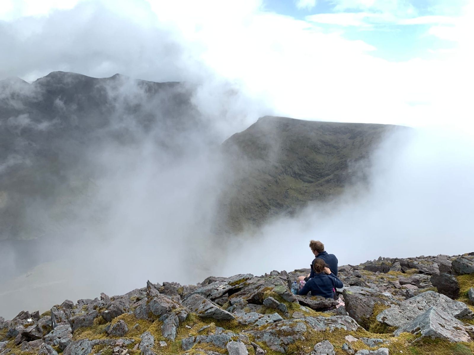A walker resting on broken rock as cloud moves across the ridge