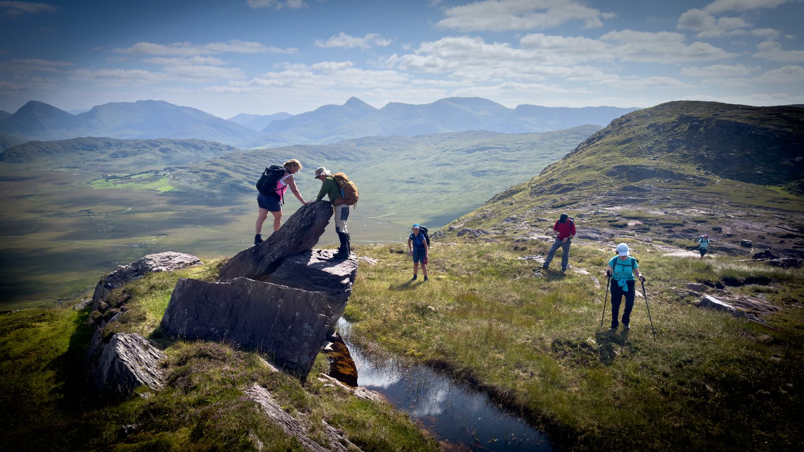 Walkers crossing rocky mountain ground beside a small pool