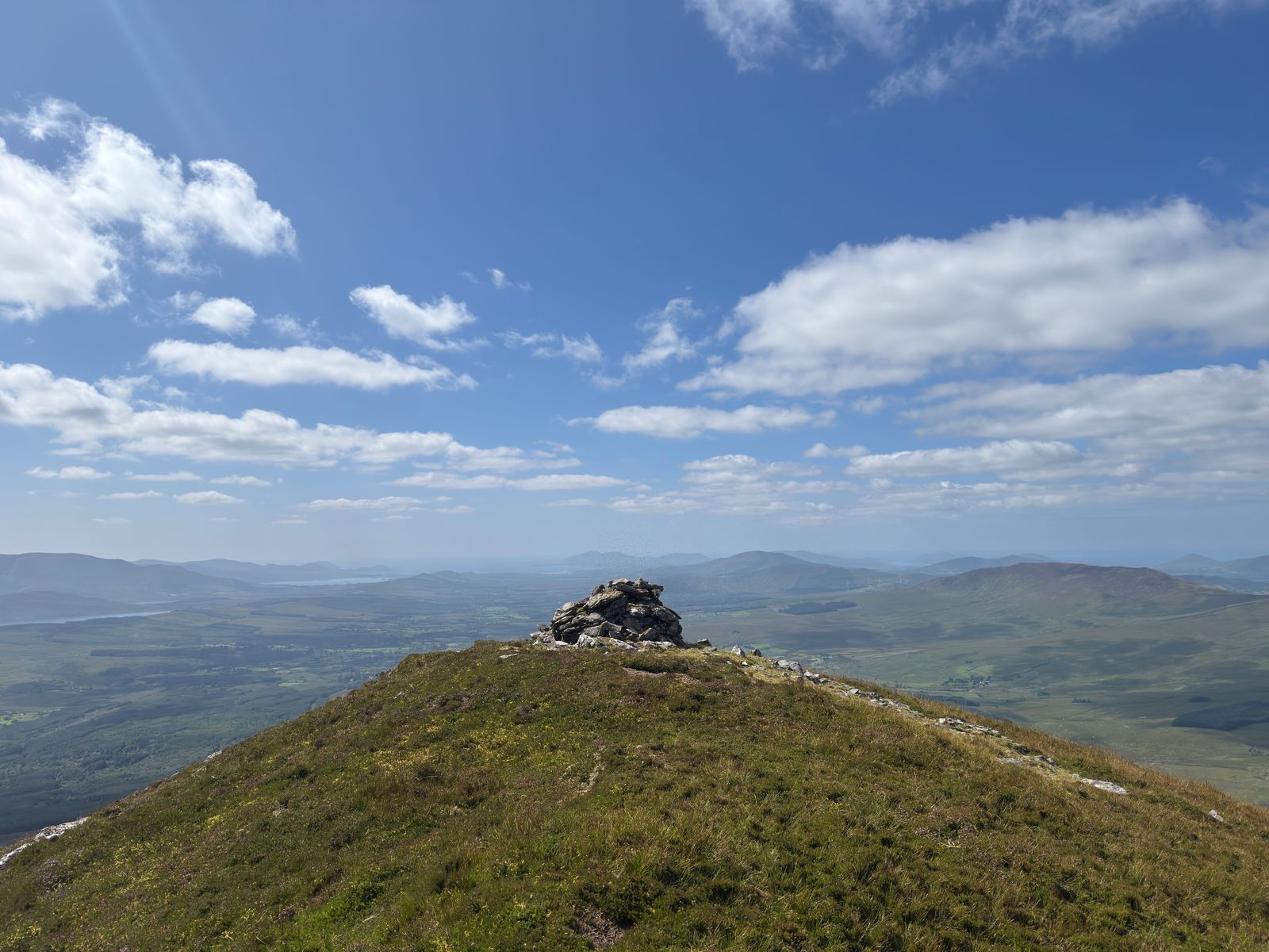 A small stone cairn on a grassy summit with distant lowlands beyond