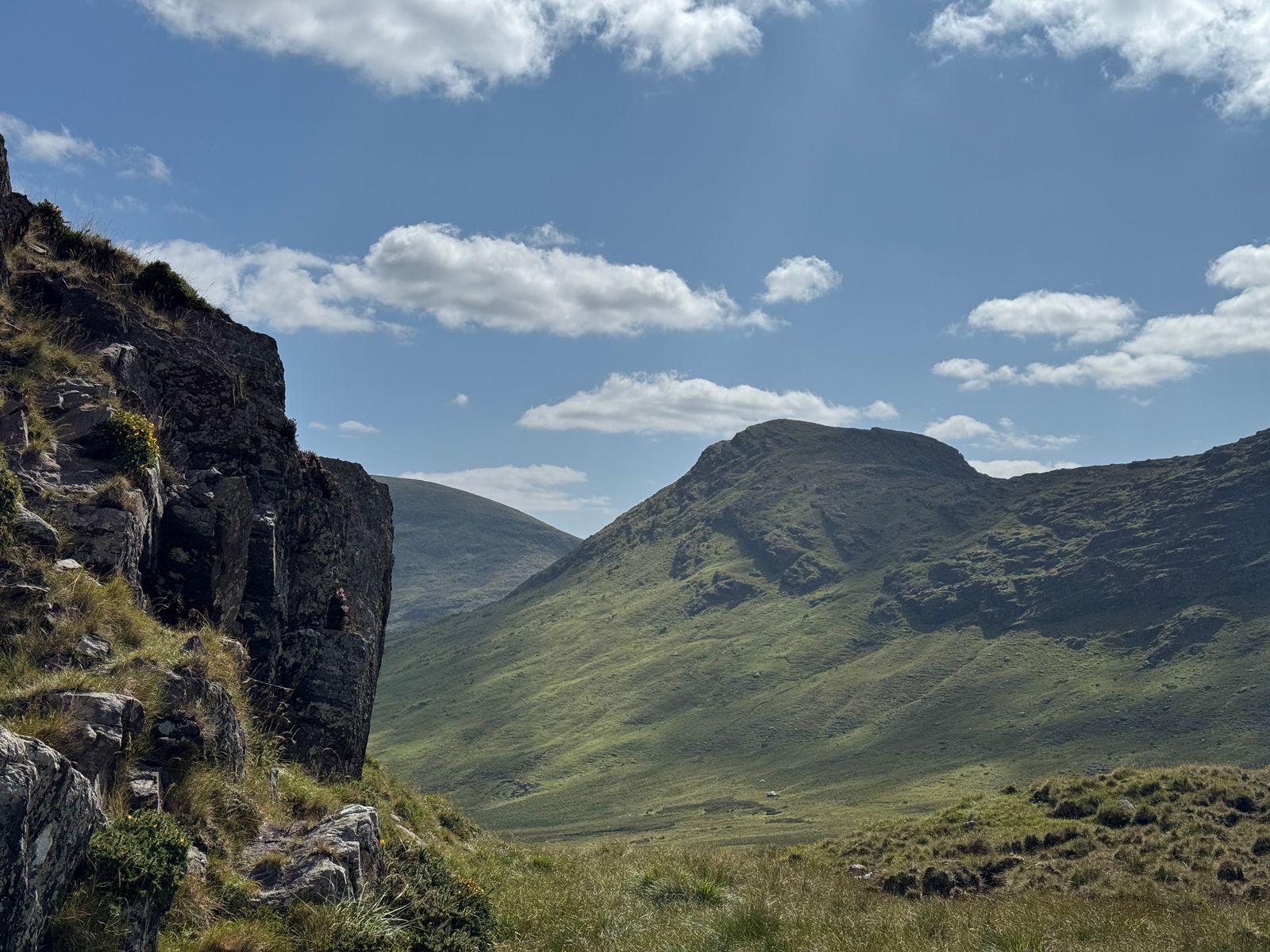 A steep rocky outcrop framing the green mountain slopes beyond