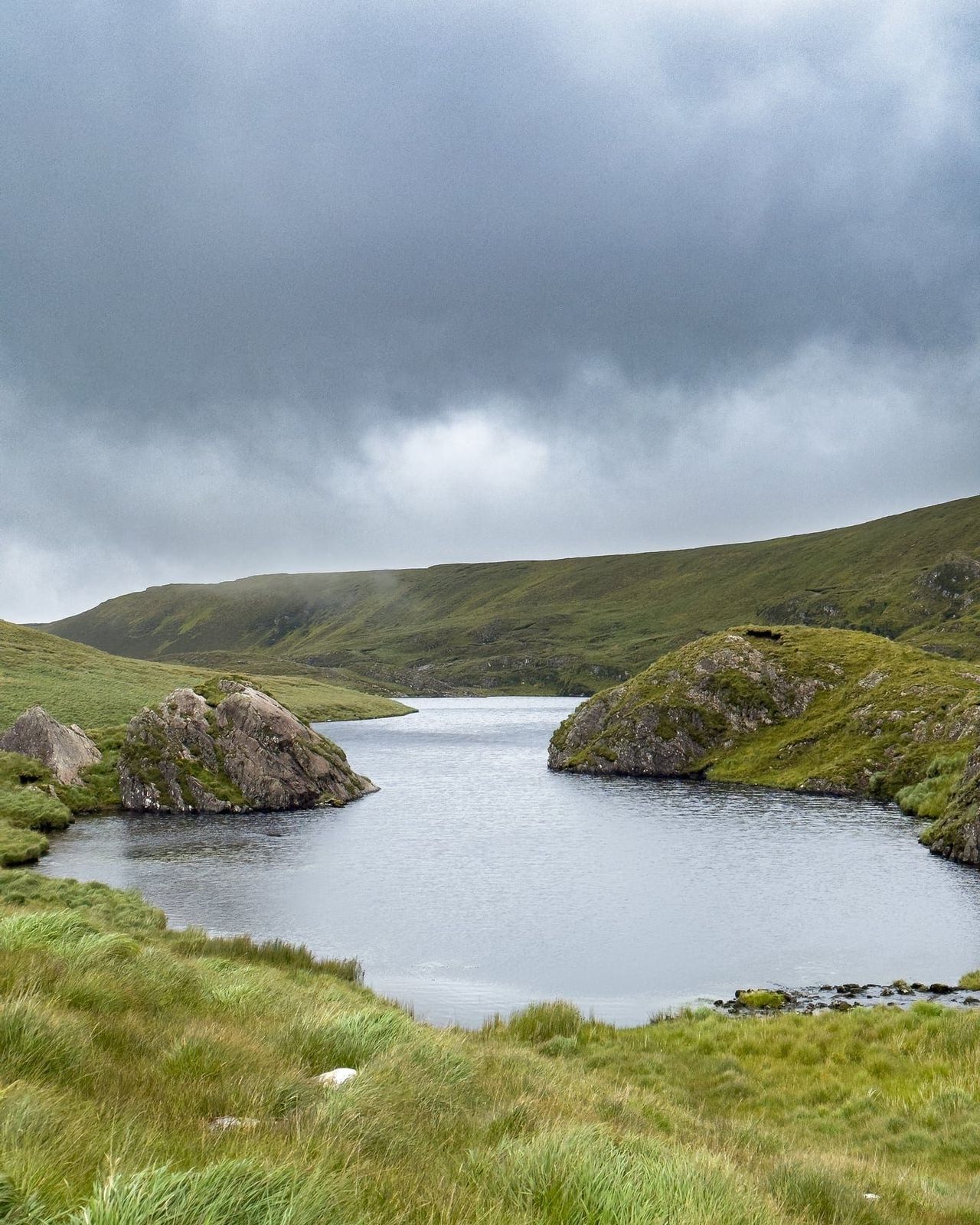 A mountain lake and rocky islands beneath a dark incoming sky
