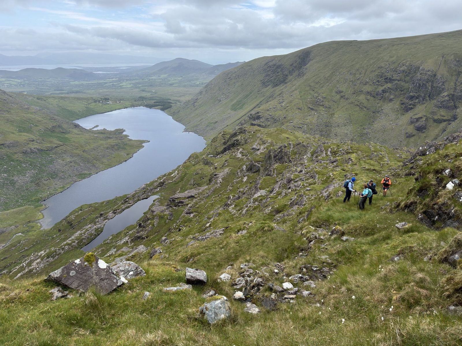 A long mountain lake viewed from a rocky traverse above its shore