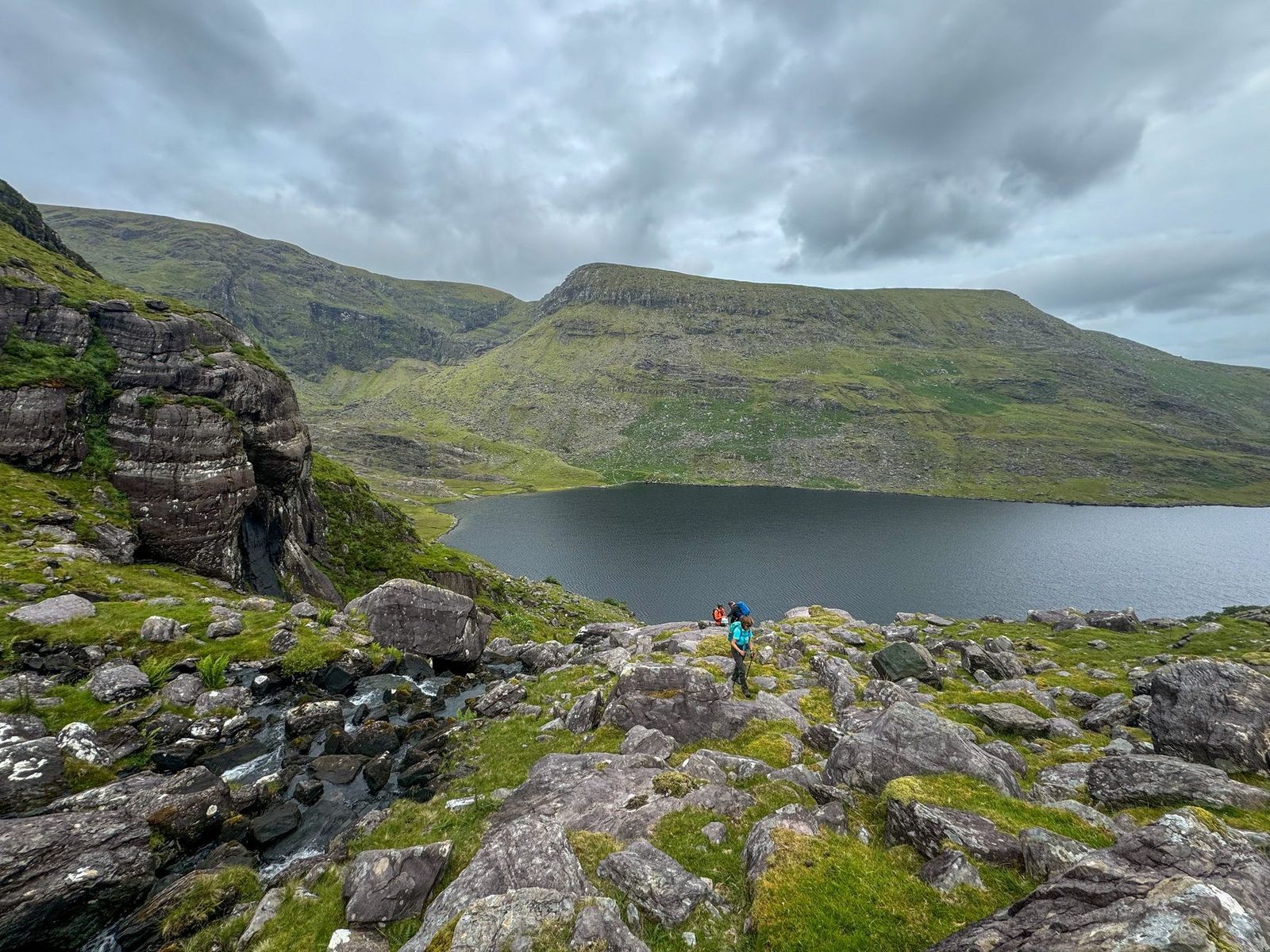 Walkers moving through broken rock above the corrie lake