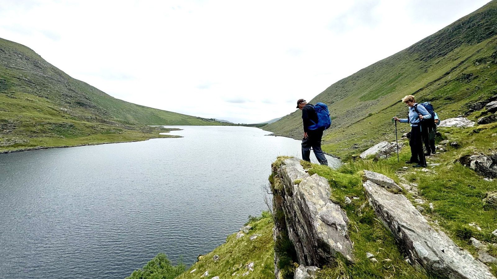Walkers standing on rock above the still edge of Coomacullen lake
