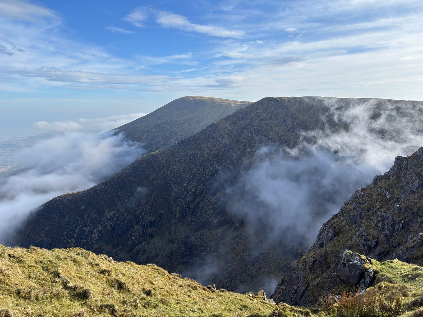Cloud curling around a dark mountain ridge beneath blue sky
