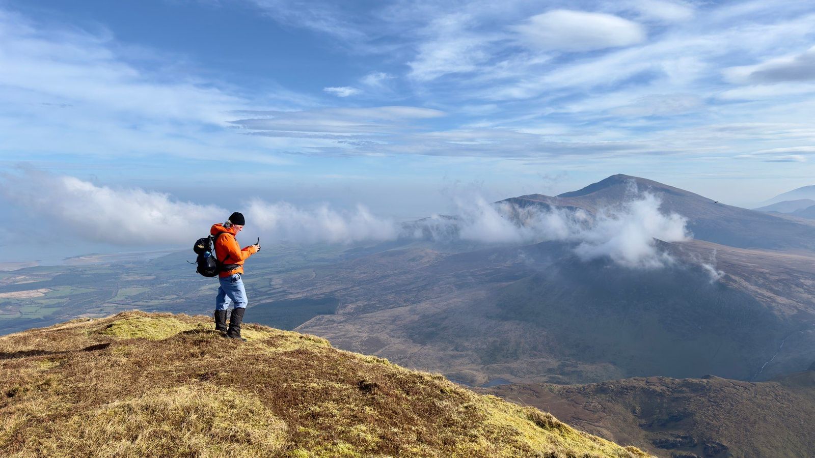 A walker in orange standing on high grass above drifting cloud