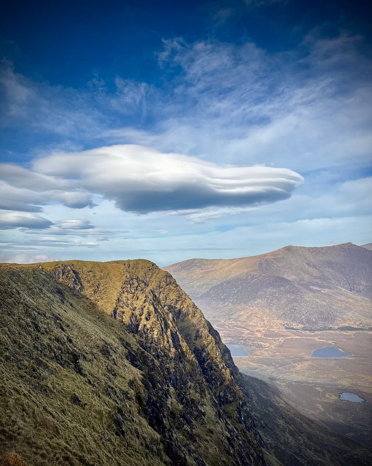 A steep corrie rim beneath layered cloud and a lenticular sky