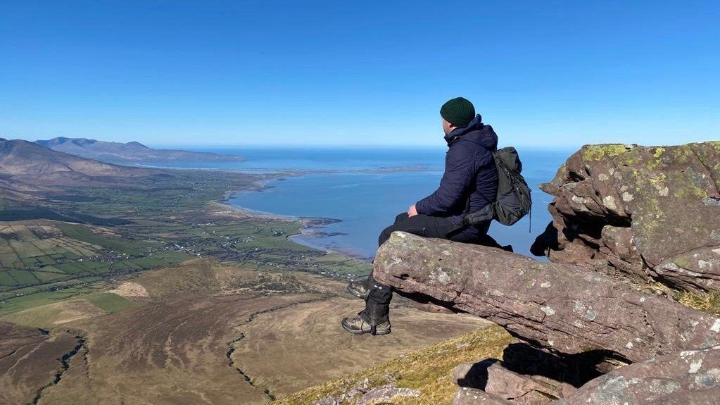 A hillwalker resting on a rock high above Tralee Bay and the north Kerry coast