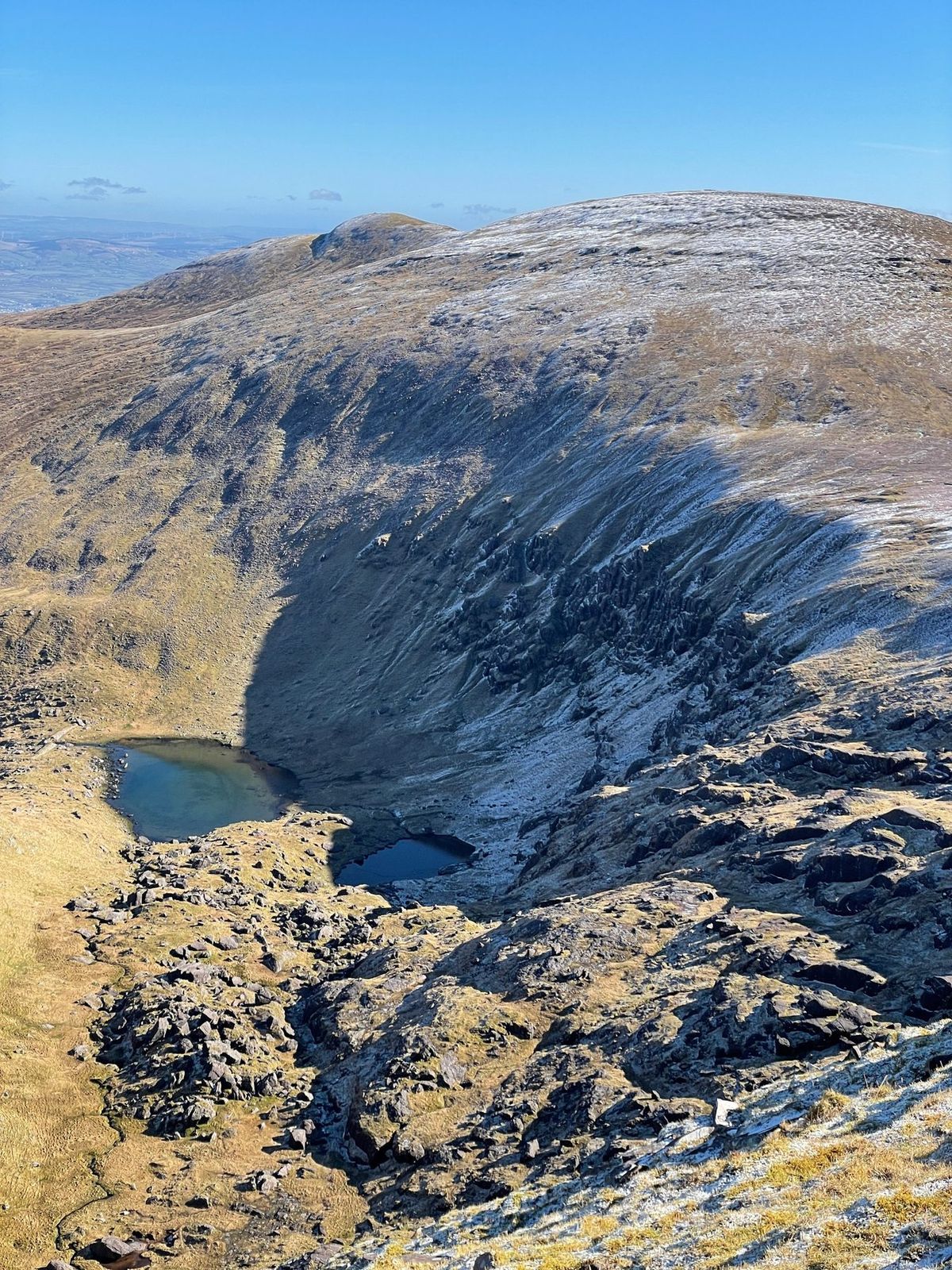 Dark corrie cliffs falling sharply towards two small mountain loughs