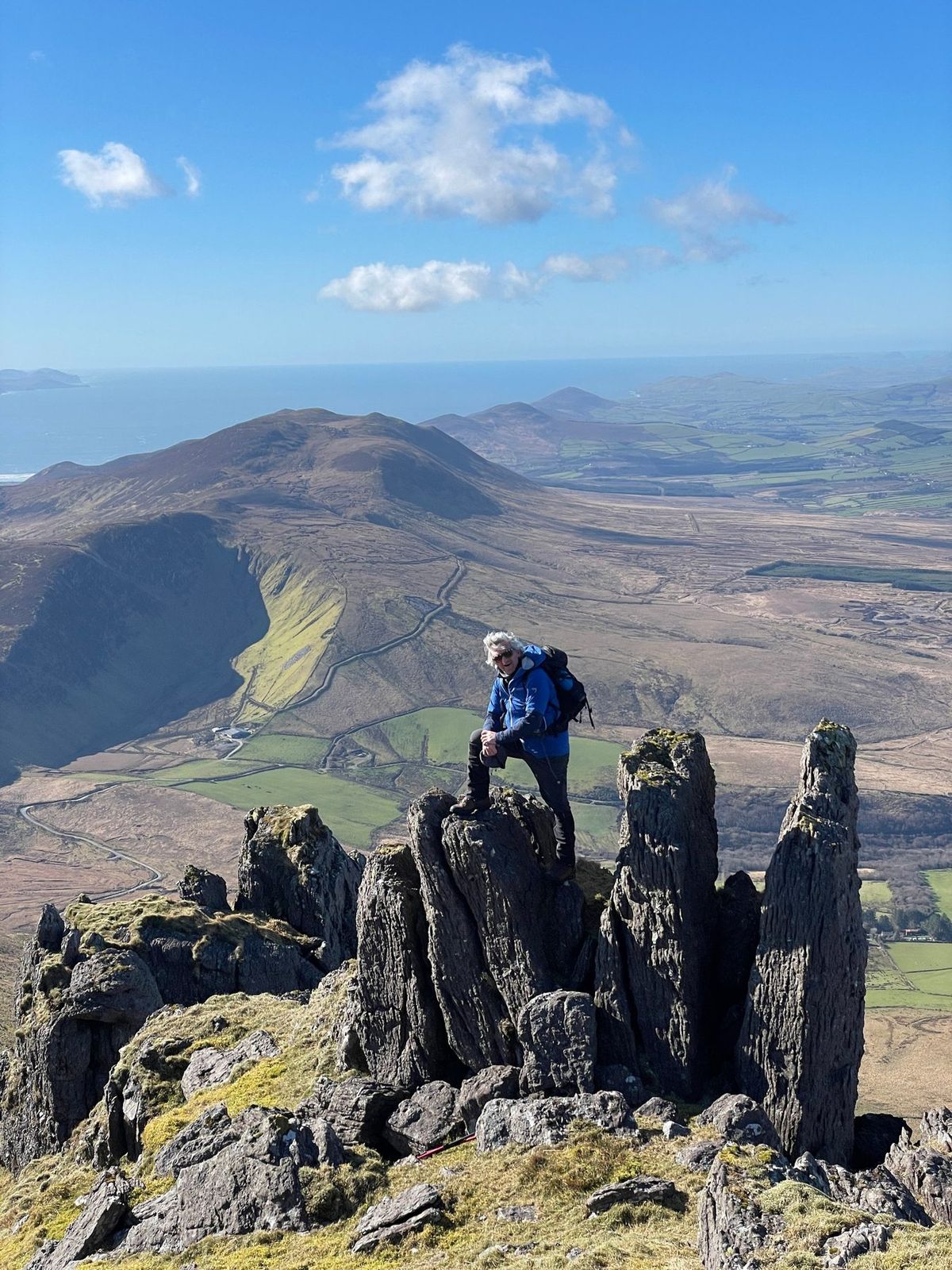 A walker crossing jagged rock with the Derrymore landscape far below