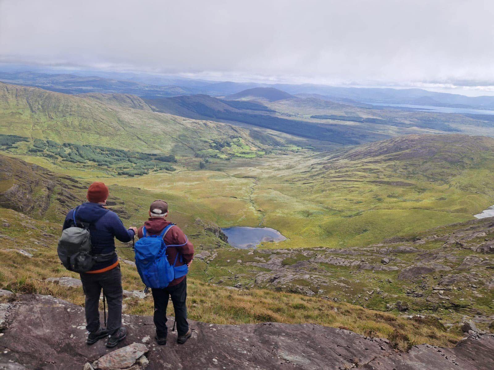 Two walkers standing on rock above a broad Iveragh valley and distant mountain ridges