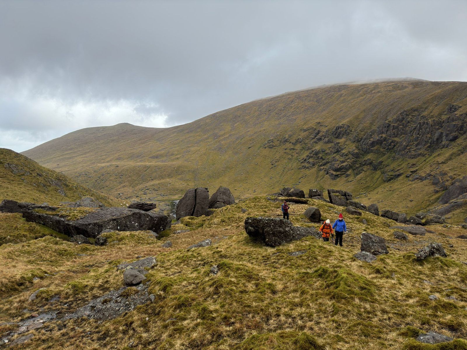 Walkers crossing rough ground among large rocks inside Derrymore Glen
