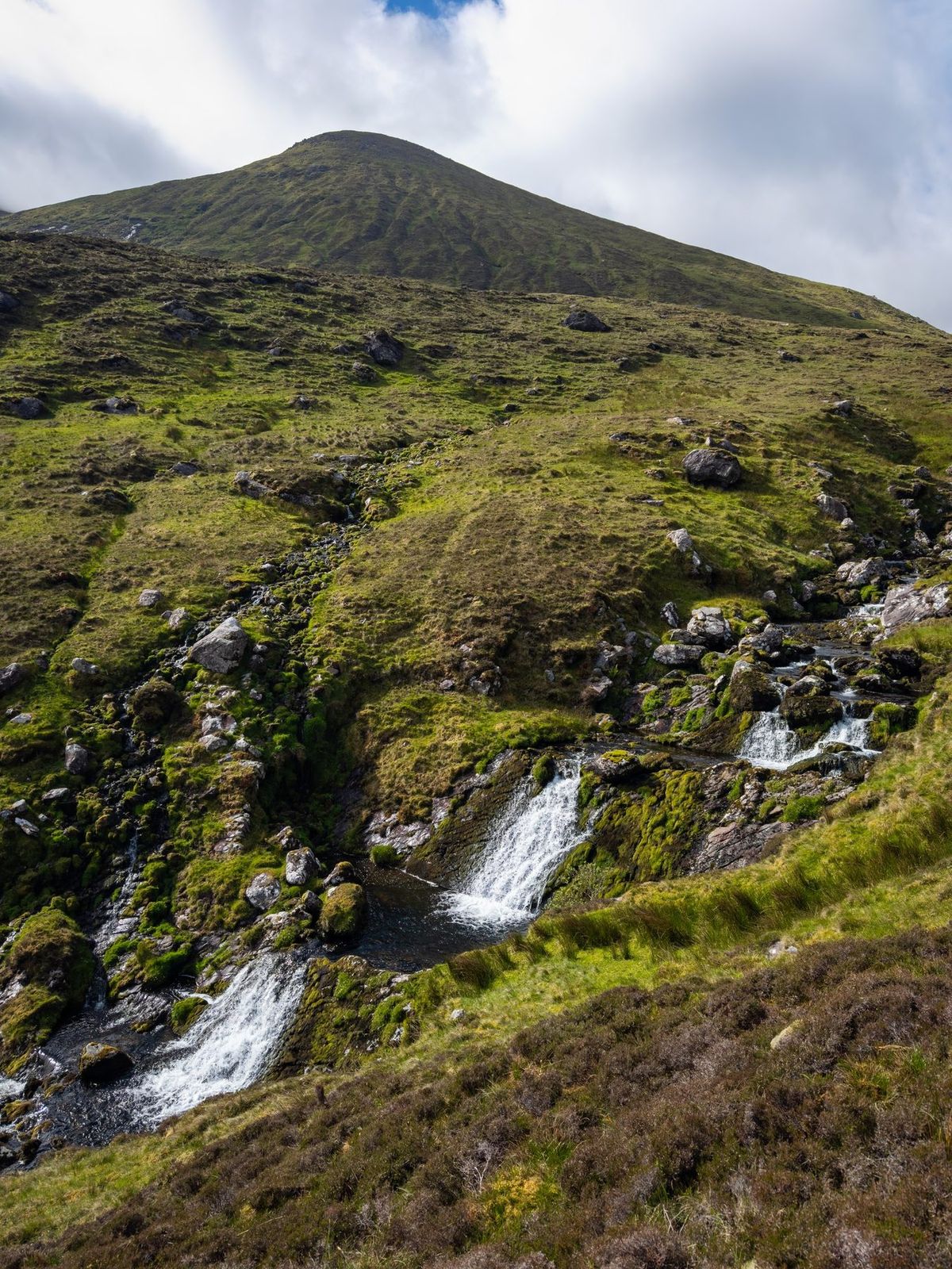 Mountain water cascading through mossy rock below a rounded Slieve Mish summit