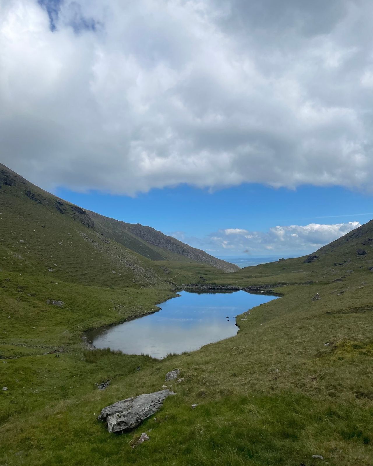 A still mountain lough reflecting blue sky between steep grassy slopes