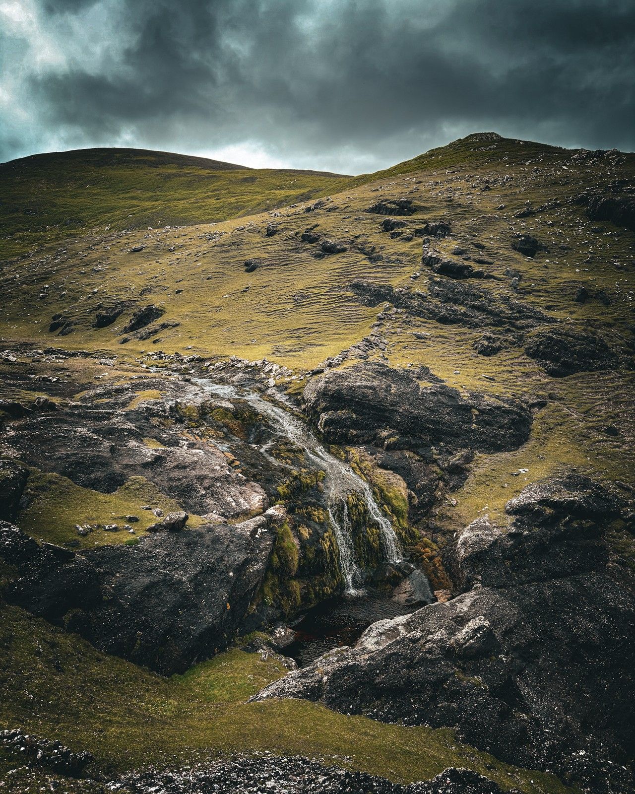 A coastal stream dropping through dark rock on the steep green cliffs towards the Atlantic