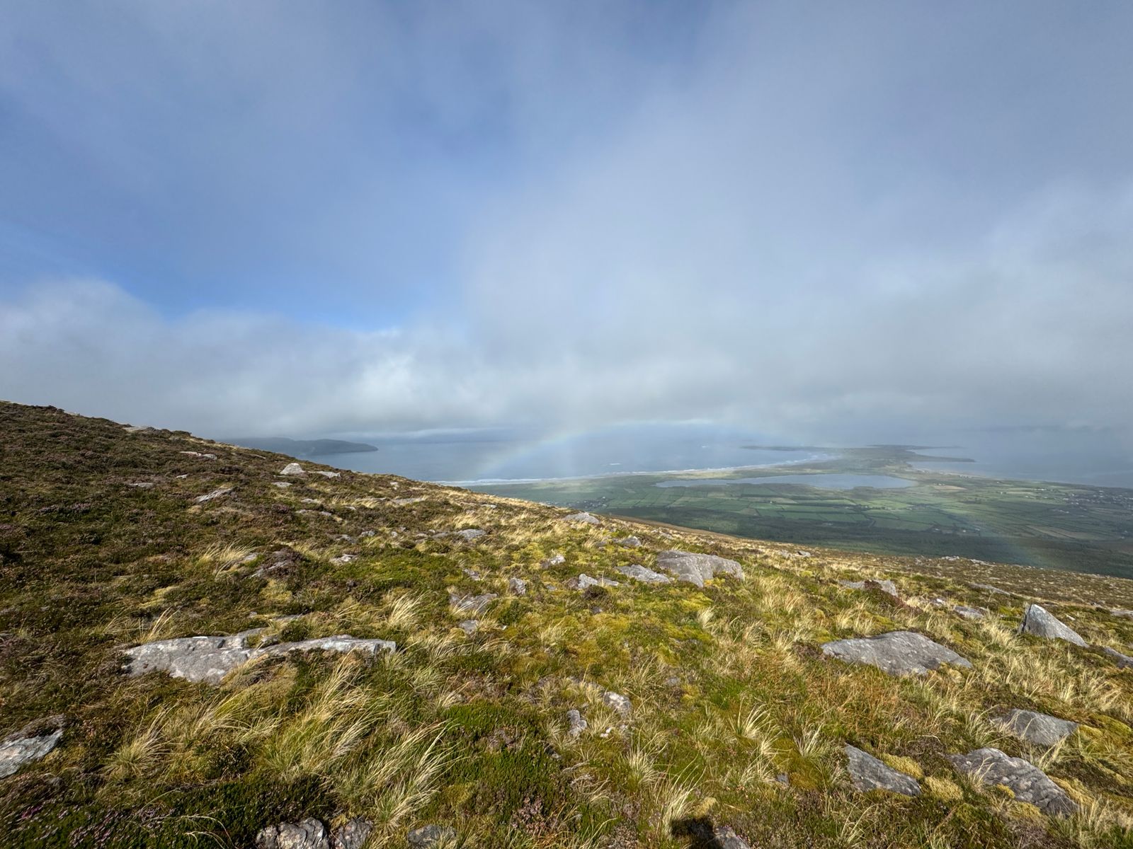 Cloud drifting across a rocky grassy slope with a faint coastal view beyond