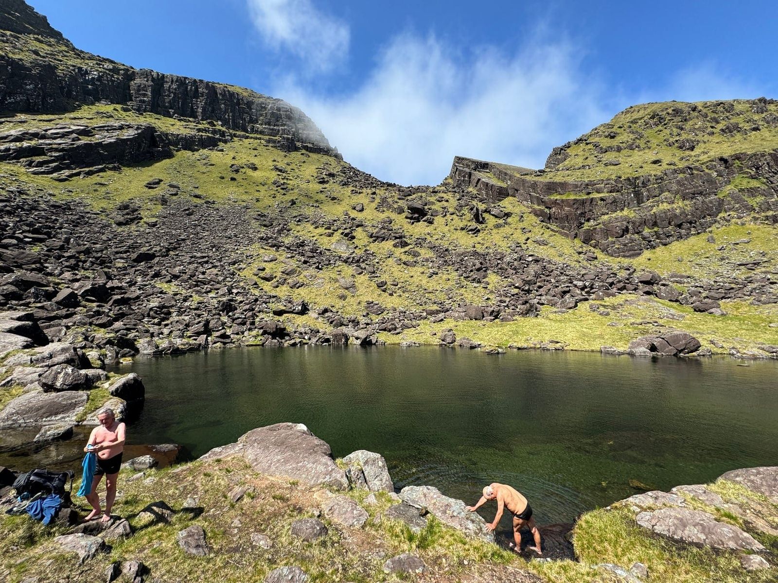 Walkers beside a dark lake enclosed by the Faha corrie