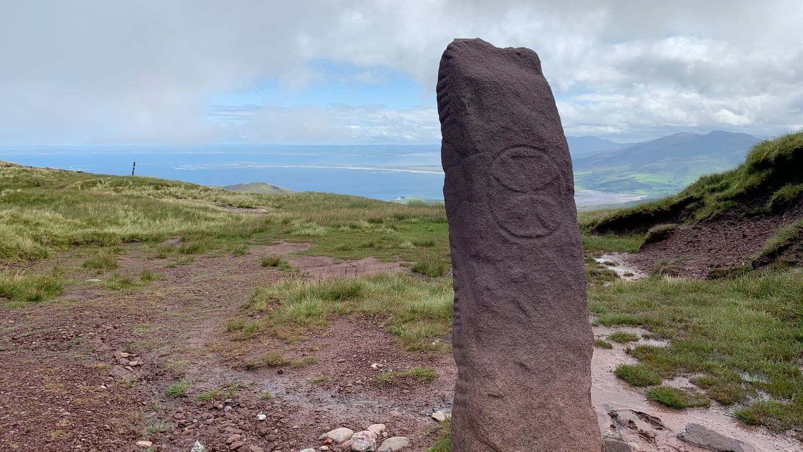 A carved stone with the Brandon coast and fields in the distance