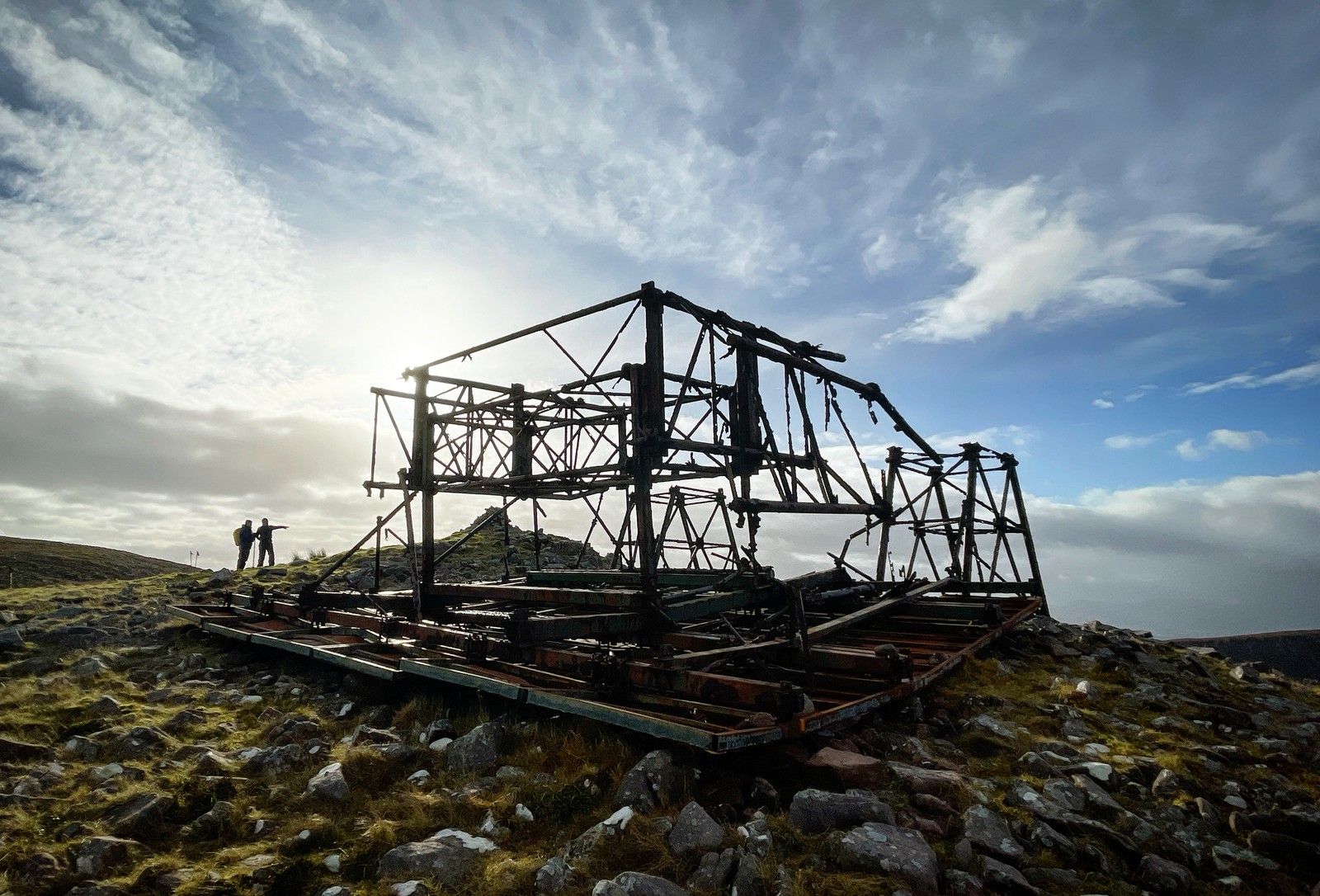 The skeletal Iron Man structure silhouetted against bright cloud with two walkers nearby