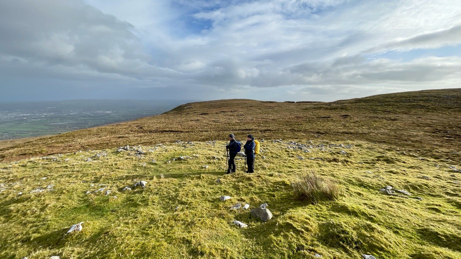 Two hillwalkers standing on open grass and stone beneath changing cloud