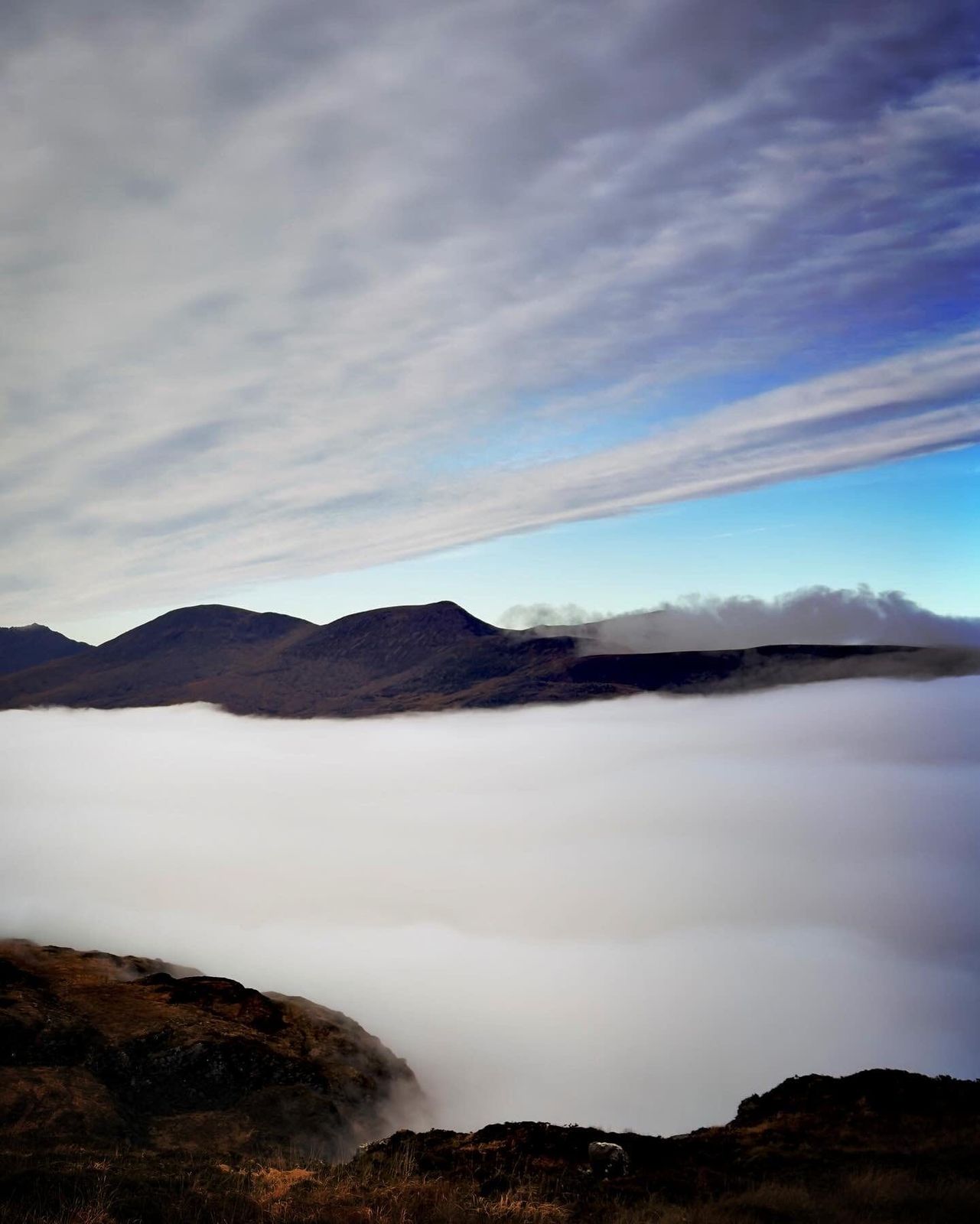 A long mountain ridge silhouetted above a smooth sea of cloud