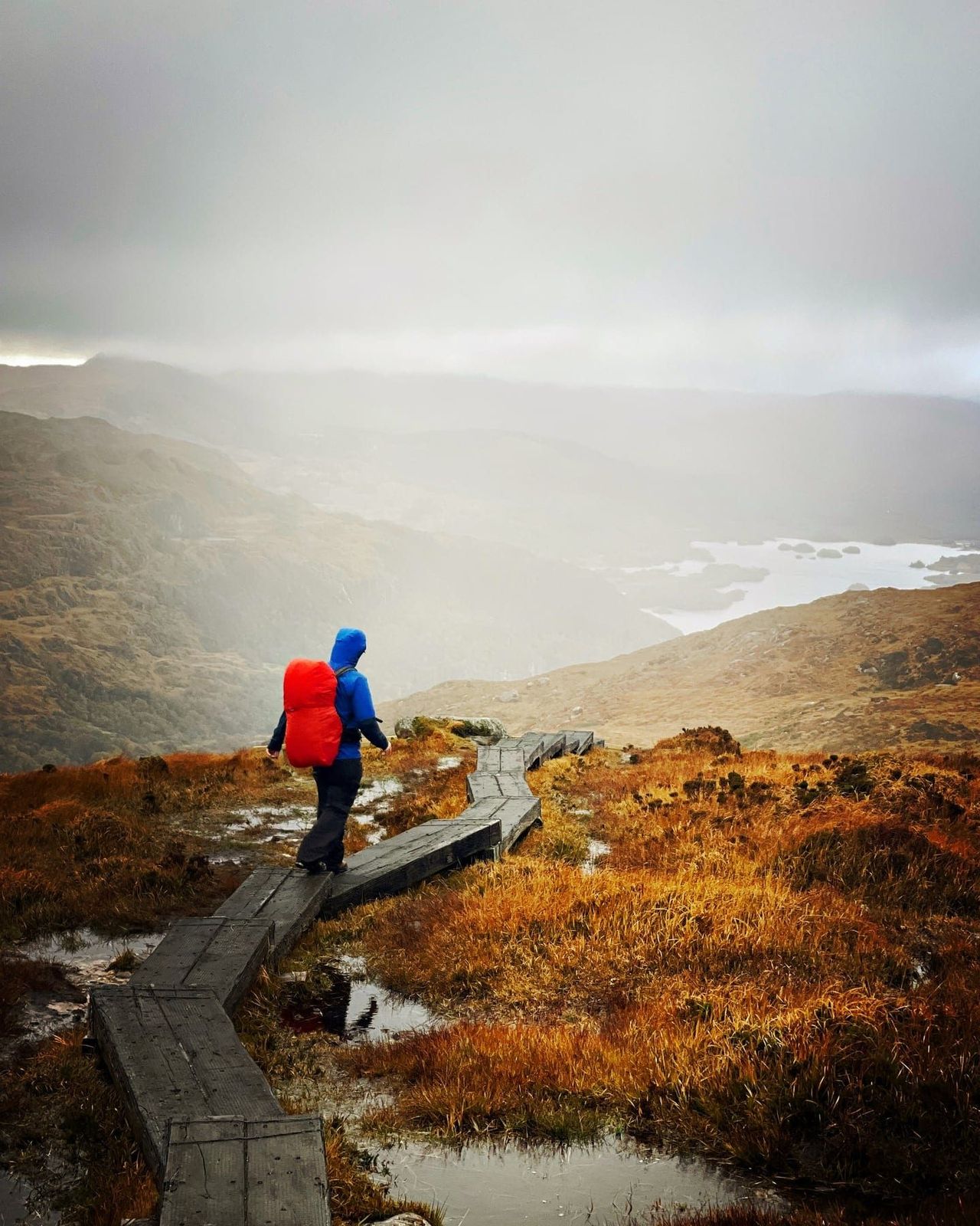 A hiker descending a mountain boardwalk in dramatic light above the lakes